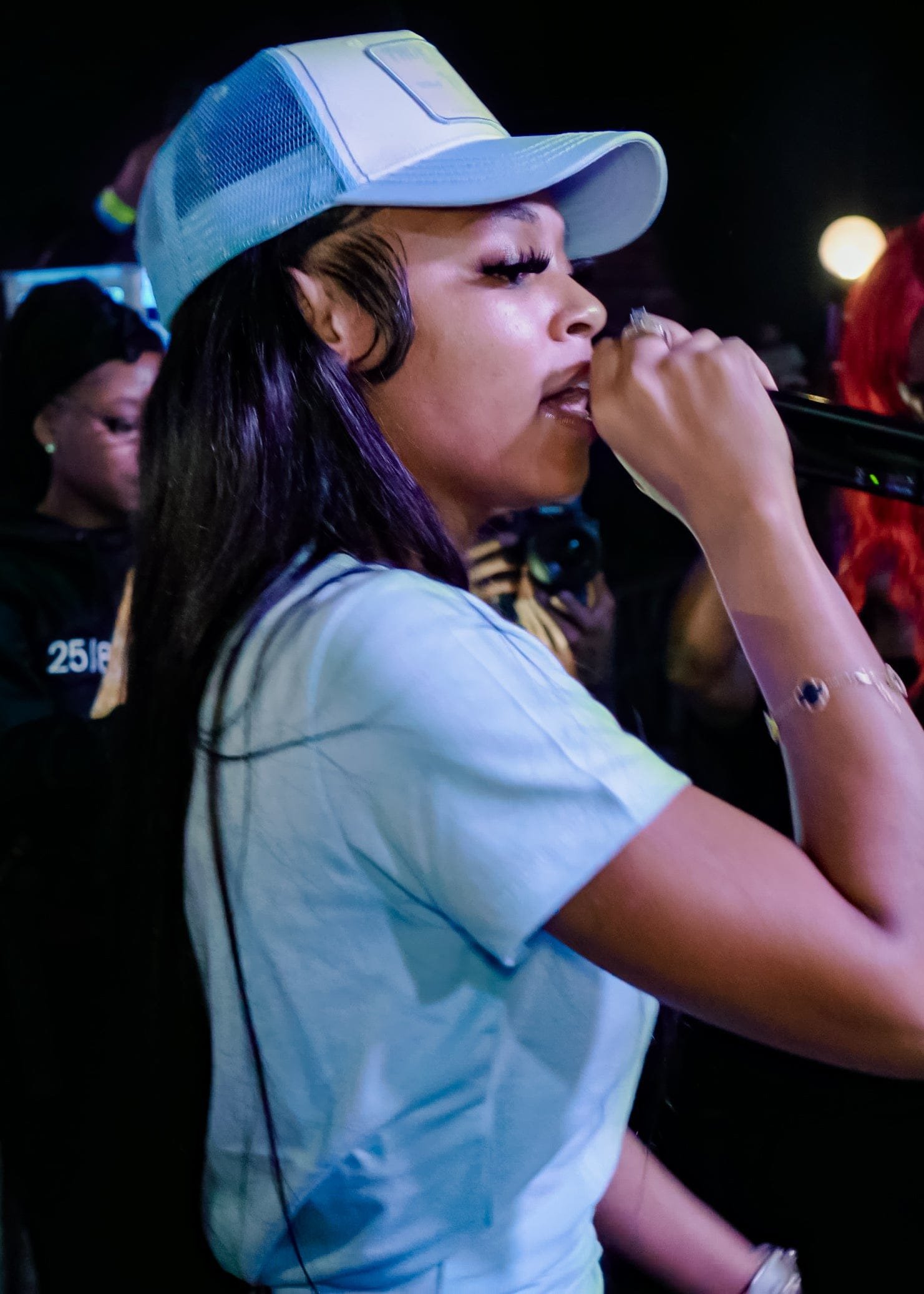 Close-up of Bigg Britt singing into a microphone at Club Skye, in a light blue trucker cap and T-shirt.